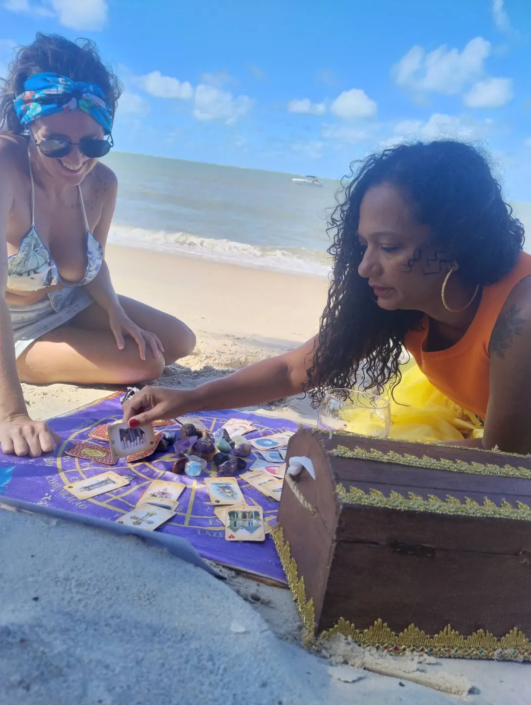 Liviã mostrando uma carta do Baralho Cigano para uma cliente sorridente durante uma consulta na praia